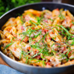BBQ chicken and bacon pasta with mature cheddar cheese and fresh basil in a pan.