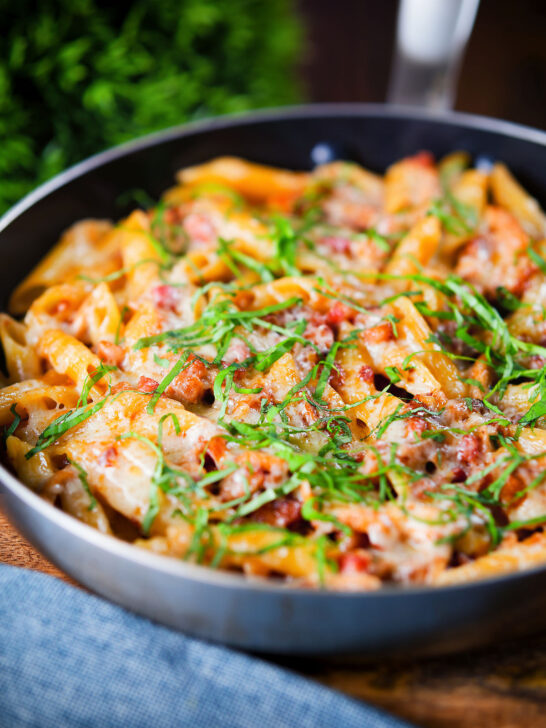 BBQ chicken and bacon pasta with mature cheddar cheese and fresh basil in a pan.
