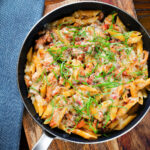 Overhead BBQ chicken and bacon pasta with mature cheddar cheese and fresh basil in a pan.