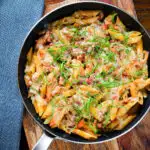 Overhead BBQ chicken and bacon pasta with mature cheddar cheese and fresh basil in a pan.