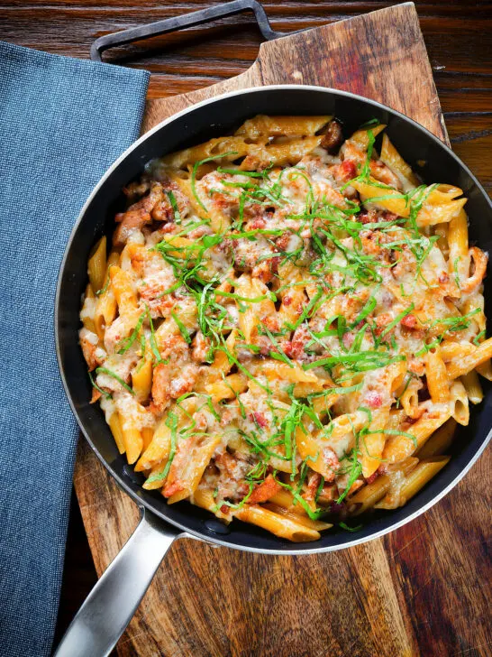 Overhead BBQ chicken and bacon pasta with mature cheddar cheese and fresh basil in a pan.