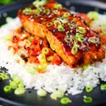 Gochujang glazed salmon fillet served with kimchi and rice garnished with spring onions and sesame seeds.
