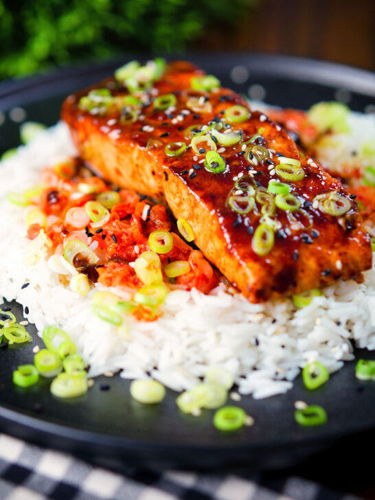Gochujang glazed salmon fillet served with kimchi and rice garnished with spring onions and sesame seeds.