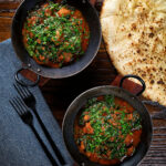 Overhead lamb saag or saagwala (lamb and spinach curry) with naan and coriander.