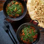 Overhead lamb saag or saagwala (lamb and spinach curry) with naan and coriander.