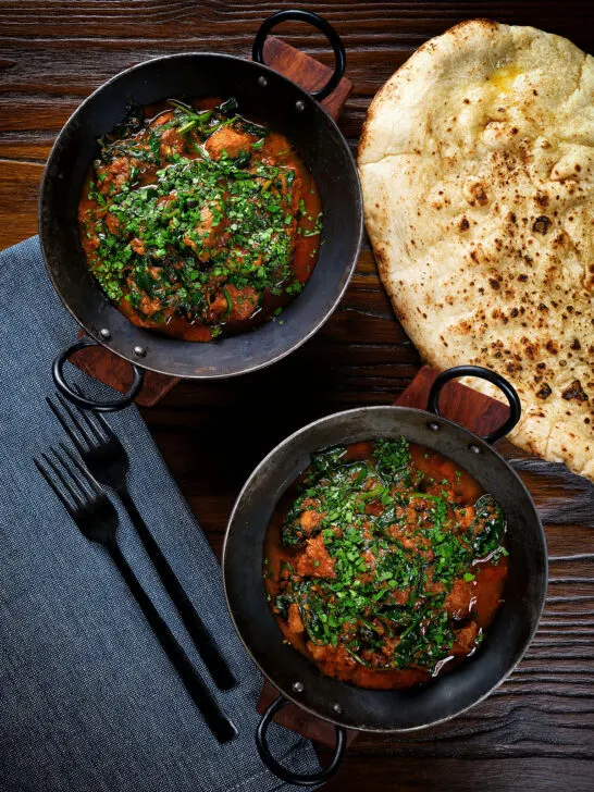Overhead lamb saag or saagwala (lamb and spinach curry) with naan and coriander.