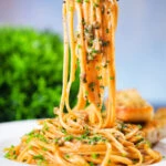 Miso butter pasta with pecorino, black & pink peppercorns and chives being lifted on a fork.