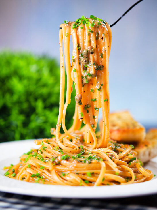 Miso butter pasta with pecorino, black & pink peppercorns and chives being lifted on a fork.