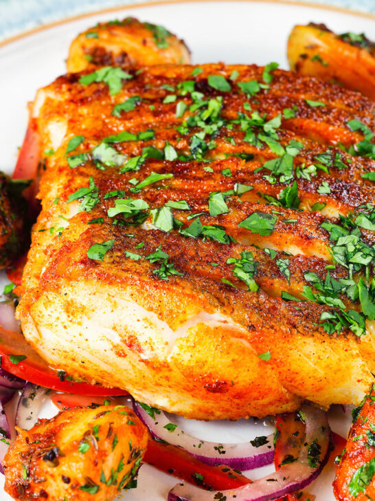 Close-up pan fried curried cod fillet with cumin potatoes and tomato & onion salad.