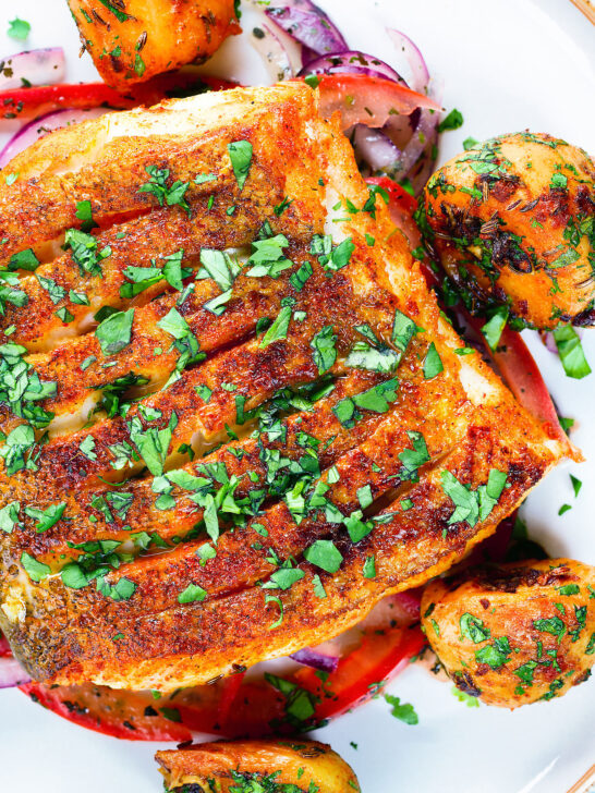 Close-up overhead pan fried curried cod fillet with cumin potatoes and tomato & onion salad.