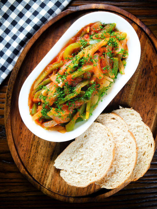 Overhead Basque piperade a pepper, onion and tomato stew garnished with parsley and served with bread.