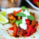 Spicy Mexican influenced halloumi cheese and vegetable fajitas with lime wedges.