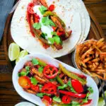 Overhead spicy Mexican influenced halloumi cheese and vegetable fajitas with lime wedges.
