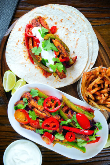 Overhead spicy Mexican influenced halloumi cheese and vegetable fajitas with lime wedges.