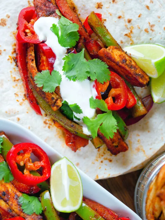 Overhead Close up Mexican influenced halloumi cheese and vegetable fajitas with lime wedges.