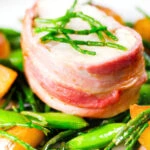 Close-up bacon wrapped monkfish with potatoes, samphire and sugar snap peas in butter and cider.