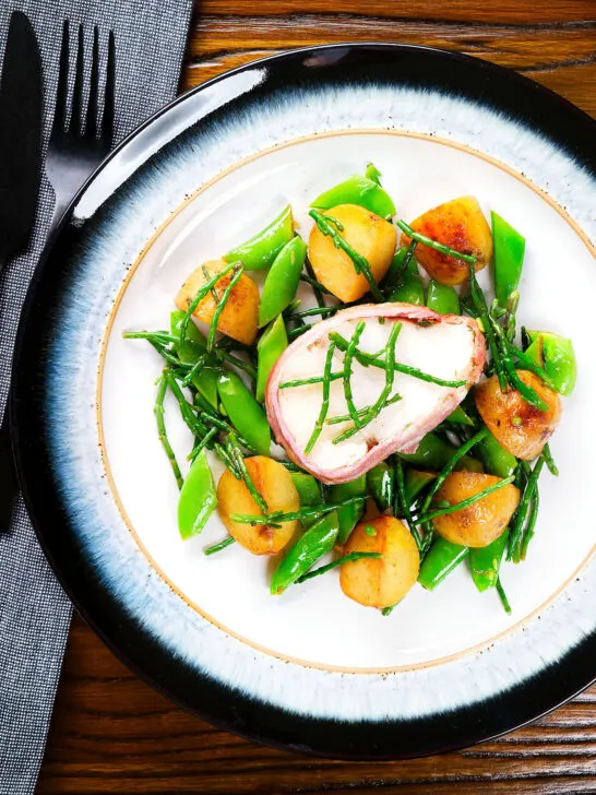 Overhead bacon wrapped monkfish with potatoes, samphire and sugar snap peas in butter and cider.