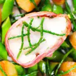 Close-up overhead bacon wrapped monkfish with potatoes, samphire and sugar snap peas in butter and cider.
