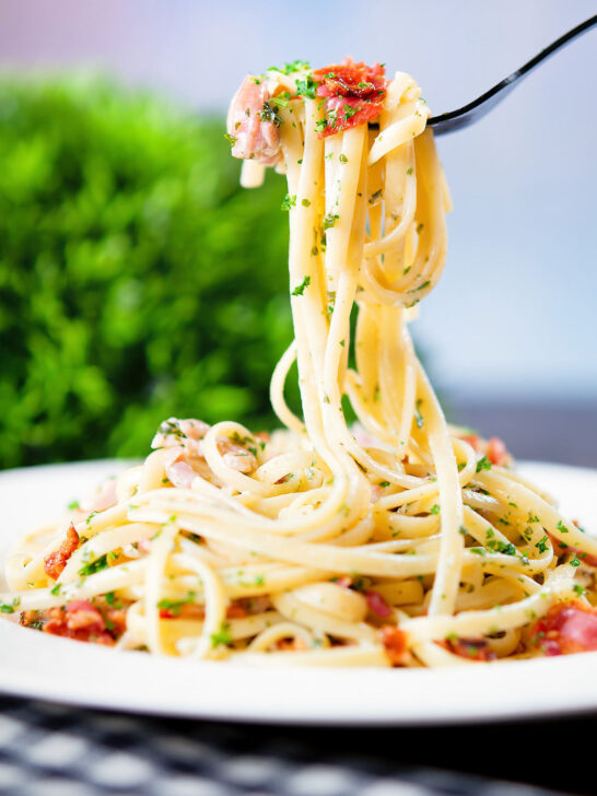 Chicken and crispy bacon pasta (linguine) in a creamy white wine sauce on a fork.