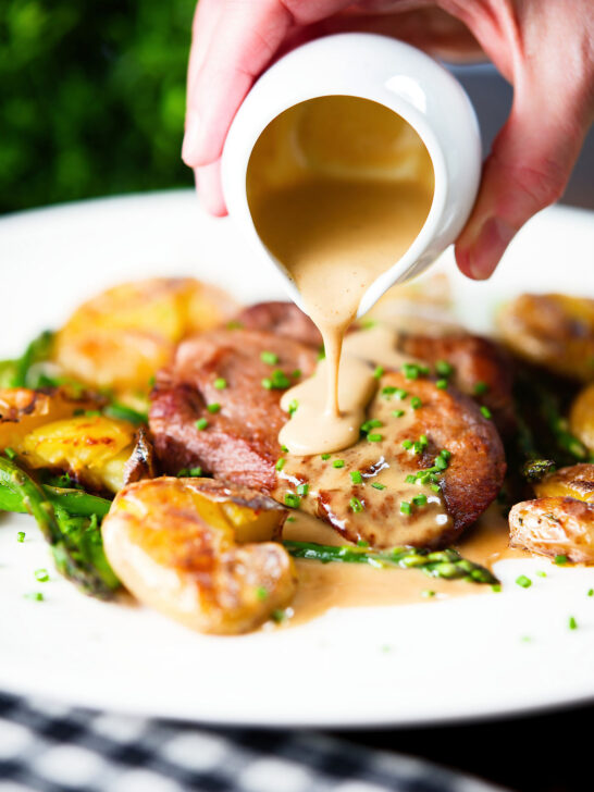 Close-up pork tenderloin medallions with a cider, mustard and camembert sauce, new potatoes and asparagus.