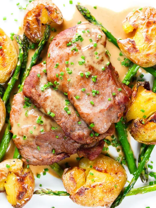 Overhead close-up pork tenderloin medallions with a cider, mustard and camembert sauce, new potatoes and asparagus.
