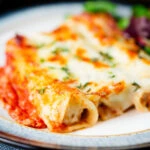 Close-up baked three cheese, pork sausage, leek and ricotta stuffed cannelloni served with a side salad.