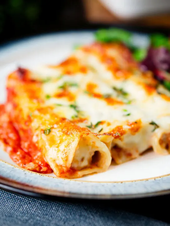Close-up baked three cheese, pork sausage, leek and ricotta stuffed cannelloni served with a side salad.