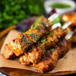 Spanish Pinchos morunos (pork skewers) served with a parsley salsa and potato wedges.