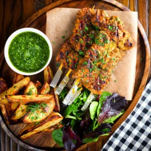 Spanish Pinchos morunos (pork skewers) served with a parsley sauce and potato wedges.