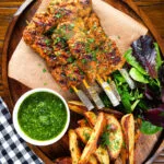 Overhead Spanish Pinchos morunos (pork skewers) served with a parsley salsa and potato wedges.