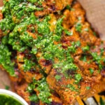 Overhead close-up Spanish Pinchos morunos (pork skewers) served with a garlic & parsley salsa.