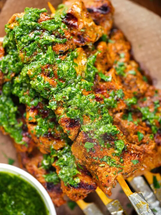 Overhead close-up Spanish Pinchos morunos (pork skewers) served with a garlic & parsley salsa.