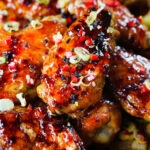 Close-up teriyaki glazed chicken wings with, chilli, spring onions, sesame seeds and French fries.