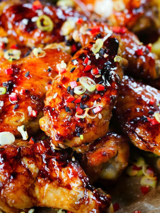 Close-up teriyaki glazed chicken wings with, chilli, spring onions, sesame seeds and French fries.
