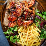 Overhead teriyaki glazed chicken wings with, chilli, spring onions, sesame seeds and French fries.