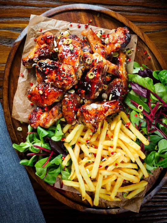 Overhead teriyaki glazed chicken wings with, chilli, spring onions, sesame seeds and French fries.