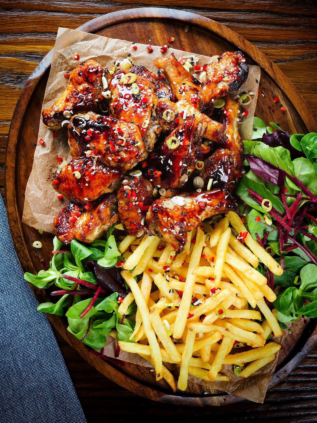 Overhead teriyaki glazed chicken wings with, chilli, spring onions, sesame seeds and French fries.