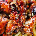 Close-up overhead teriyaki glazed chicken wings with, chilli, spring onions, sesame seeds and French fries.