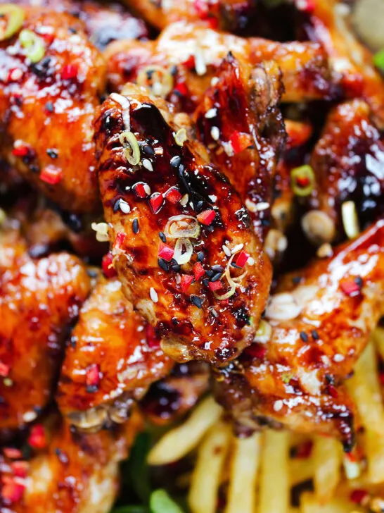 Close-up overhead teriyaki glazed chicken wings with, chilli, spring onions, sesame seeds and French fries.