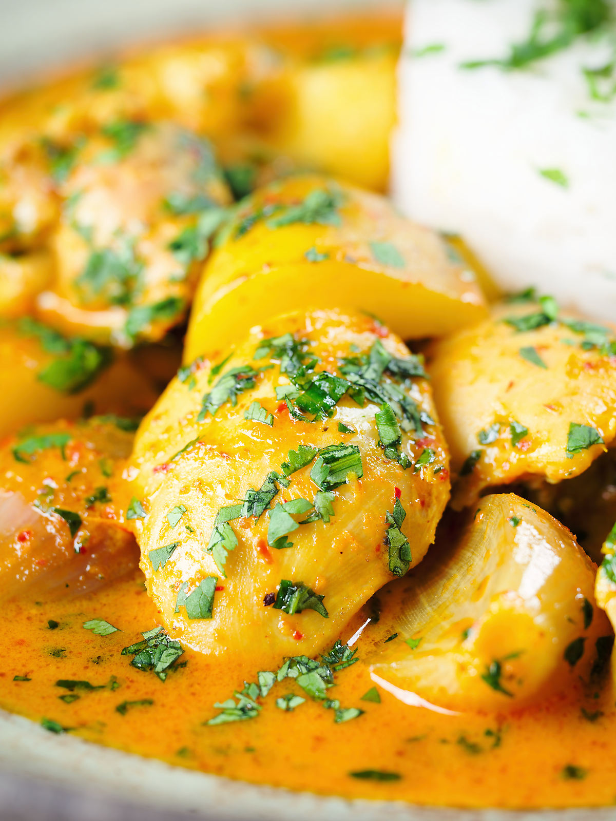 Close-up Thai yellow chicken curry with new potatoes, shallots, steamed jasmine rice and coriander.
