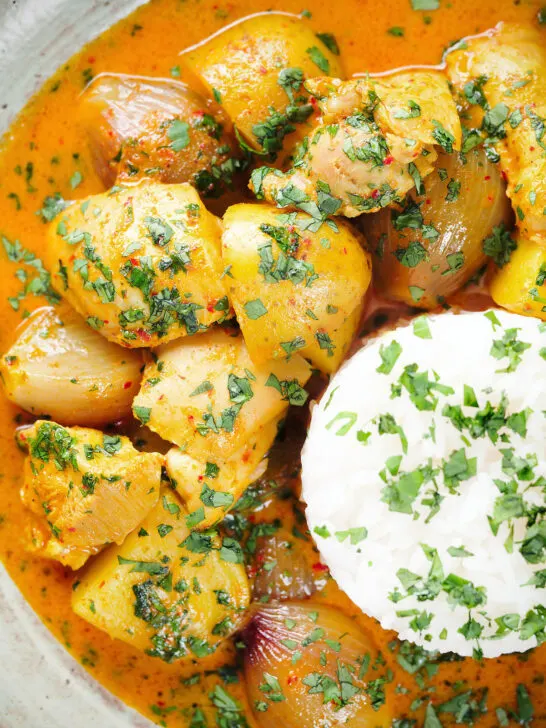 Overhead close-up Thai yellow chicken curry with new potatoes, shallots, steamed jasmine rice and coriander.