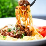 Beef pastitsada (Corfu) served with linguine pasta being eaten with a fork.