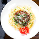 Overhead beef pastitsada (Corfu) served with linguine pasta and tomato and parmesan.