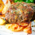 Close-up baked Greek bifteki patties with lemon roasted potatoes and salad.