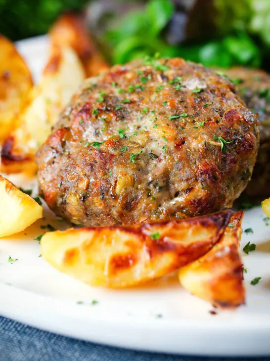 Close-up baked Greek bifteki patties with lemon roasted potatoes and salad.