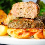 Cut-open Greek bifteki patties with lemon roasted potatoes and salad.