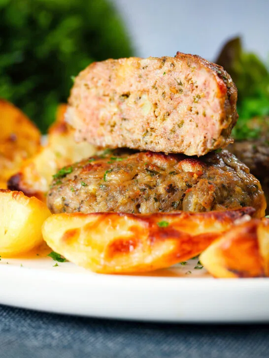 Cut-open Greek bifteki patties with lemon roasted potatoes and salad.