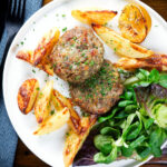 Overhead baked Greek bifteki patties with lemon roasted potatoes and salad.