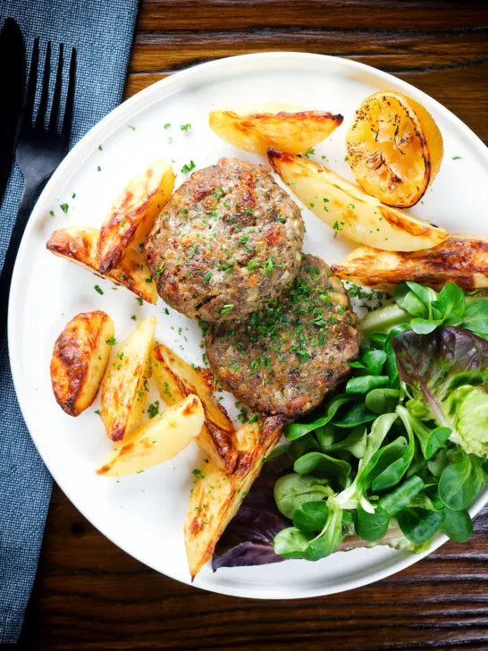 Overhead baked Greek bifteki patties with lemon roasted potatoes and salad.