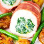 Close-up chicken wrapped in Parma ham stuffed with spinach and ricotta served with roasted new potatoes and green beans.